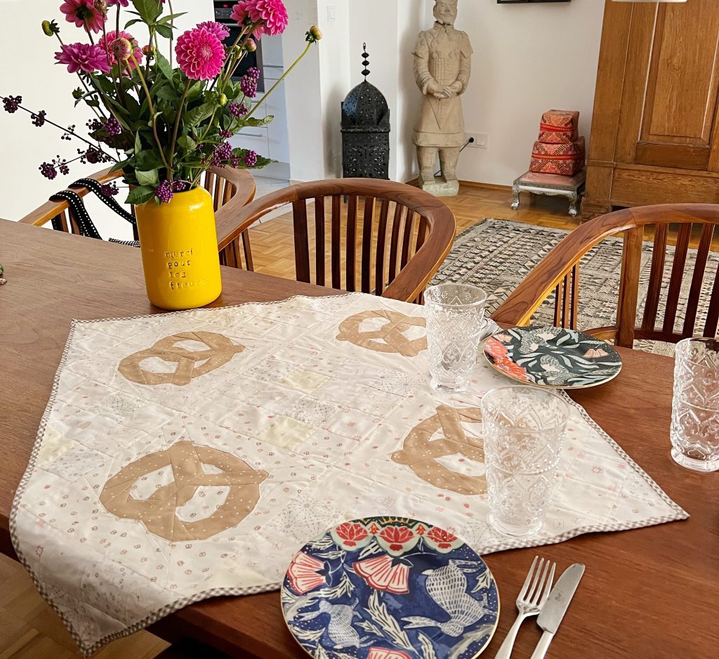 Esstisch mit Brezel Tischdecke, bunte Teller, Gläser und ein Blumenstrauß