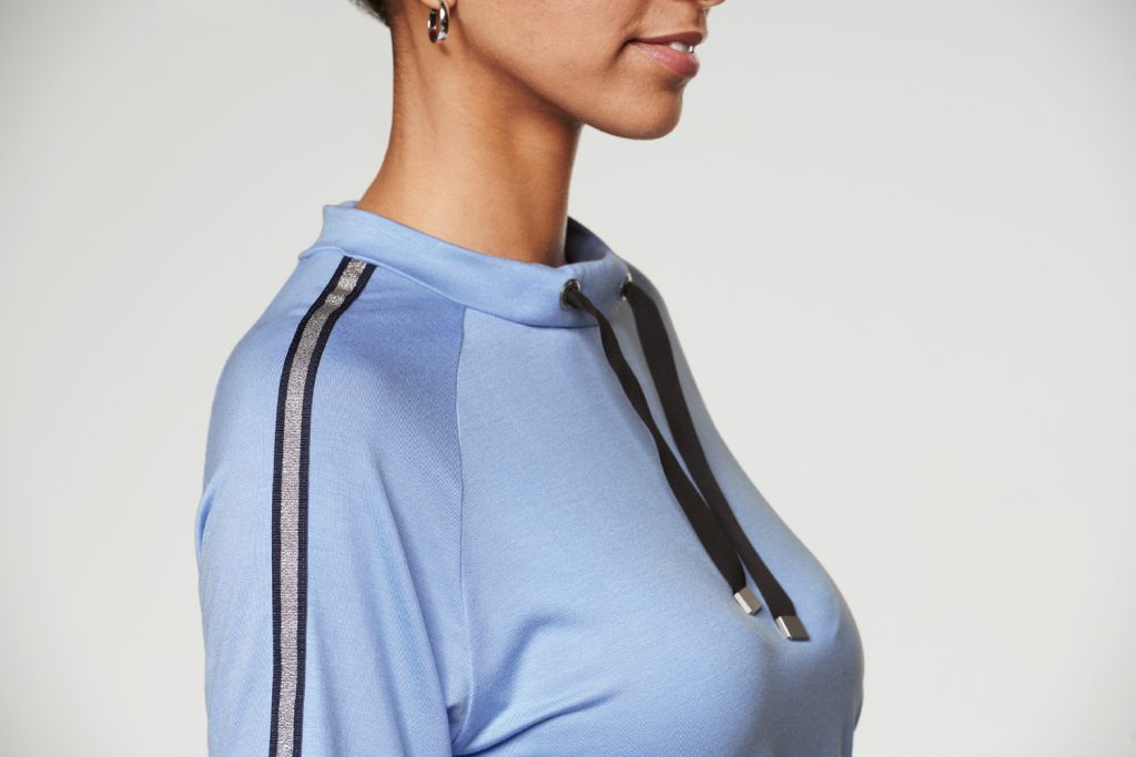 Model wearing a skyblue tshirt with sleeves reaching the hight of her ellbows, with a silver stripe fom ellbow to shoulder. The Shirt also has a black cord around the neck. 